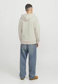 Lys grå hætte sweatshirt med en afslappet pasform, kombineret med løse blå denimjeans og brune sko. Simpelt design uden synlige mønstre.