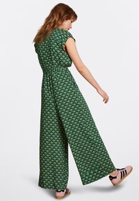 Grön jumpsuit med blommönster, korta ärmar, åtdragen midja och vida ben. Outfit kompletteras med skor i rosa och svart.