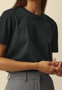 T-shirt nera in cotone con maniche corte e collo rotondo, abbinata a pantaloni grigi sartoriali. Texture liscia, design minimale e senza motivi visibili.