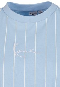 Lyseblå t-skjorte med korte ermer, vertikale hvite striper og brodert "Kani"-logo. Mykt bomullsmateriale, design med rund hals.