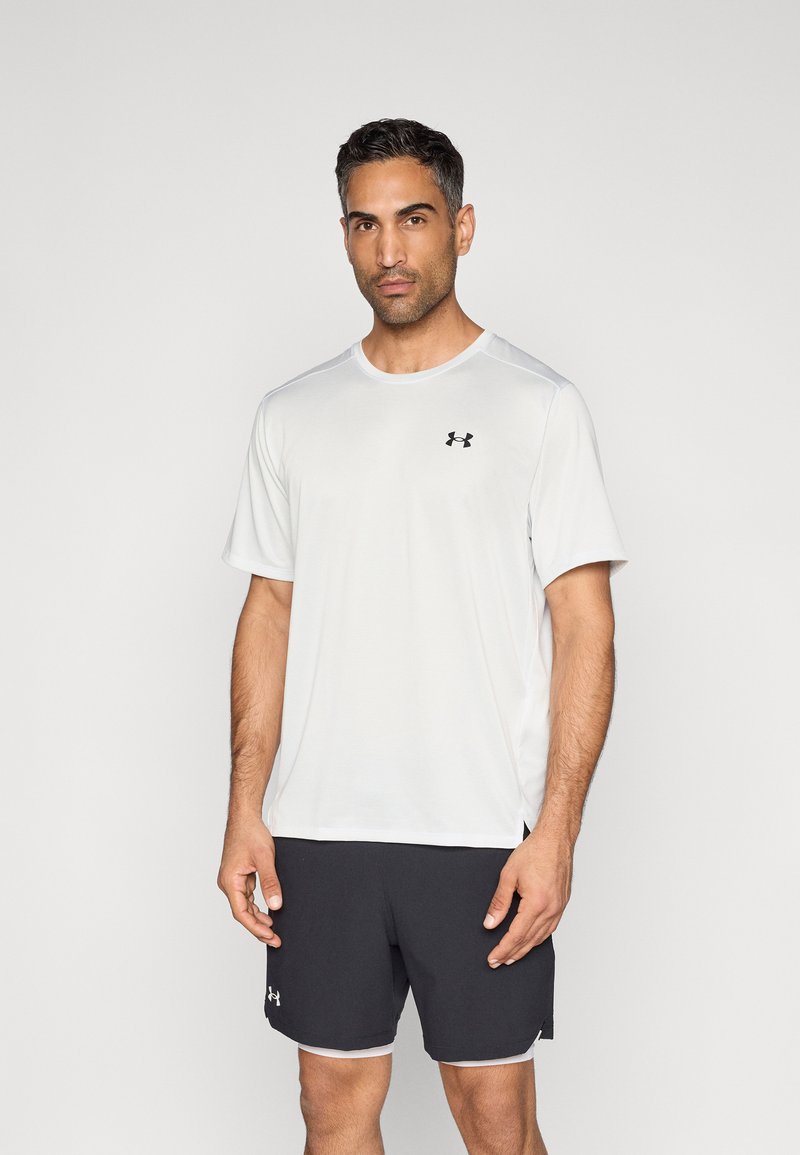 Camiseta deportiva blanca de manga corta y cuello redondo; cuenta con un pequeño logo negro en el pecho izquierdo. Combinada con pantalones cortos negros.