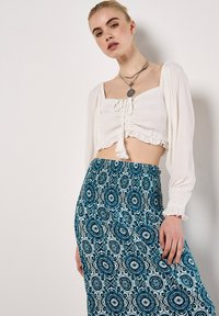 Vit cropped topp med rynkdetaljer och knytband, kombinerad med en lång kjol som har ett blått och svart blommönster.