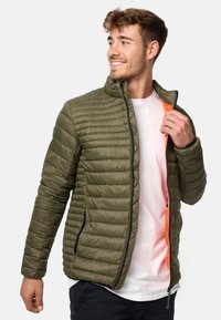 Grøn quilted puffer jakke med sorte lynlåse og orange indvendigt. Har en opretstående krave og to sidelommer.