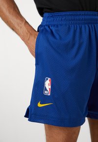 Kék hálós kosárlabda nadrág hímzett NBA logóval és sárga Nike pipa emblémával az oldalon. Rugalmas derékrész a kényelem érdekében.