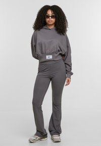 Szary krótki hoodie z przyszywanym sznurkiem i naszywką z logo, w połączeniu z dopasowanymi spodniami w kształcie dzwonów. Materiał wydaje się miękki i gładki, idealny na codzienne noszenie.