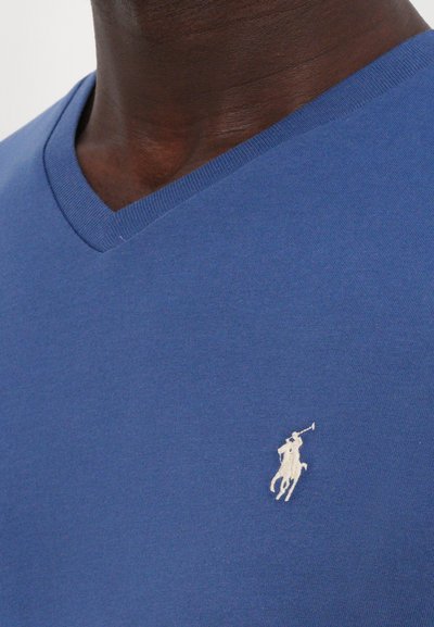 Zila V veida t-kreklu, izgatavotu no mīksta kokvilnas, ar mazu baltu polo spēlētāja logotipu kreisajā krūtī un gludu tekstūru.