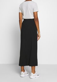 Jupe longue noire avec une taille élastique, associée à un haut à manches courtes rayé gris et blanc et des chaussures de sport blanches.