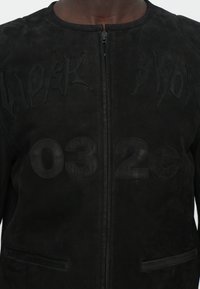 Fekete velúr dzseki, amelyen a "WORK" és "032C" felirat domborúan van kialakítva az elején, strukturált dizájn, magas nyakkal és cipzáras záródással.