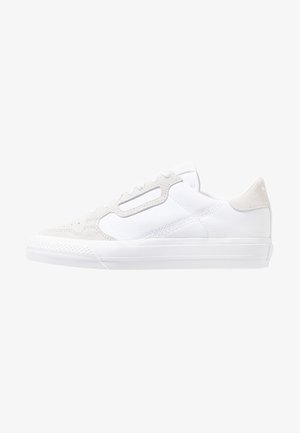 Witte lage sneaker met suède accenten, veters aan de voorkant en een gestructureerde rubberen zool, zijaanzicht op een witte achtergrond.