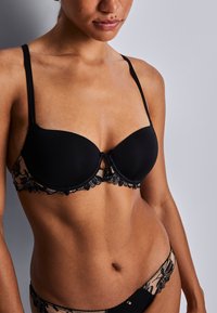 Soutien-gorge rembourré noir avec des détails en dentelle transparente, doté de fines bretelles ajustables et d'accents floraux décoratifs le long de la bande et des bords.