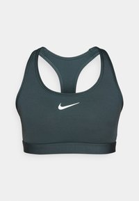 Tumši zaļš sporta krūšturis ar gludu tekstūru, sacensību muguras dizainu un baltu Nike logo priekšpusē. Tas ir pieguļošs un elastīgs apakšējā daļā.