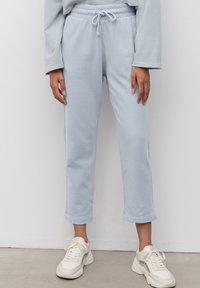 Světlé modré, zkrácené tepláky vyrobené z měkké látky s elastickým pasem a šňůrkou na stažení. Vytvořené v kombinaci s bílými teniskami se zelenými akcenty.