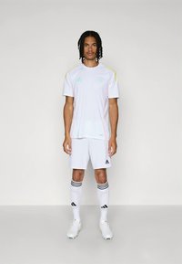 Balta futbola forma ar dzelteniem un pasteļtoņiem, ietverot apaļu kaklu, īsām piedurknēm un baltas bikses. Balti futbola zābaki un zeķes.