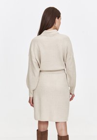 Beiges gestricktes Pulloverkleid mit strukturiertem Muster, oversized Ballonärmeln und einem taillierten Gürtel, das bis zur Mitte des Oberschenkels reicht.