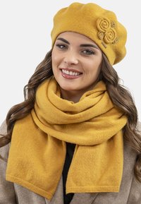 Mosterdgele wollen baret met drie stoffen rozenaccenten, gecombineerd met een bijpassende wollen sjaal, beide met een zachte, gestructureerde afwerking.