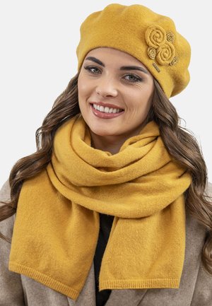 Mosterdgele wollen baret met drie stoffen rozenaccenten, gecombineerd met een bijpassende wollen sjaal, beide met een zachte, gestructureerde afwerking.
