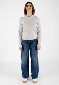 Maglione lavorato a maglia di un beige chiaro con colletto tondo, abbinato a jeans in denim blu larghi e sneaker bianche con suole marrone chiaro.