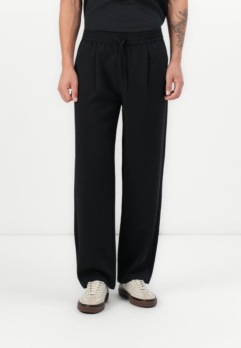 Zwarte, elastische tailleband, rechte broek met een losse pasvorm, voorzien van voorplooien en zijzakken. Gestyled met lichte sneakers.