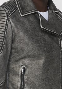 Giacca in pelle grigio metallizzato con colletto a revers, dettagli a coste sulle spalle e tasca con zip laterale.