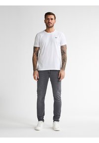 Camiseta de algodón blanca con cuello redondo, combinada con jeans de mezclilla gris ajustados. Conjunto completo con zapatillas blancas.