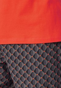 Rode katoenen shirt boven patroonachtige donkergrijze shorts met een geometrisch ontwerp met diamanten en kleine oranje accenten.