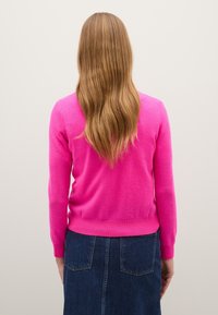 Suéter fucsia de manga larga, con cinturilla ajustada y puños acanalados, combinado con una falda de mezclilla oscura que presenta bolsillos traseros.