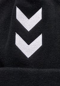 Zwarte gebreide beanie met twee witte chevronpatronen geborduurd boven de omslag. Zachte textuur met een nauwsluitend ontwerp.