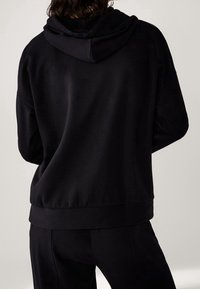 Zwarte hoodie met een textuurstof, relaxte pasvorm en geribbelde zoom. Eenvoudig ontwerp, geen zichtbare logo's en een gladde afwerking.