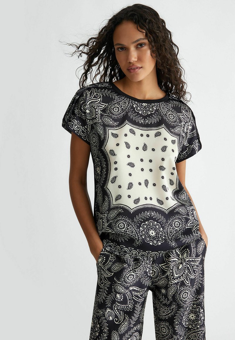 Top bianco e nero con motivo paisley, maniche corte, scollatura rotonda e una sezione centrale beige a contrasto.