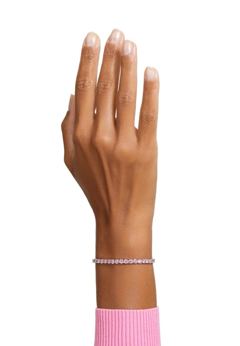 Bracciale rosa adornato con gemme rotonde, indossato su una mano con smalto per unghie neutro, su uno sfondo bianco semplice.
