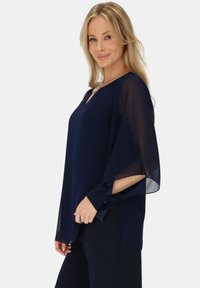 Granatowa bluzka z szyfonu z dekoltem w szpic, luźnymi rękawami motylkowymi i mankietami z zapięciem na guziki. Lekka i zwiewna tekstura.