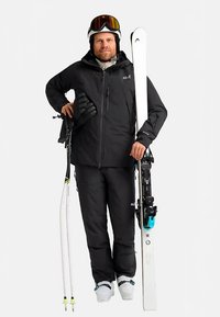 Zwart ski-jack en broek, witte ski's met gele uiteinden, skistapschoenen, handschoenen en skibril. Eenvoudig ontwerp, functionele materialen, winteruitrusting.