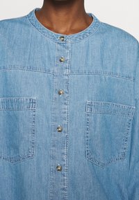 Helles blaues Jeanshemd mit Rundhalsausschnitt, Frontknöpfen und zwei Brusttaschen. Verfügt über sichtbare Nähte und einen lockeren Schnitt.