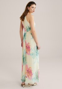 Robe maxi en tissu léger avec un motif floral pastel. Caractérisée par un corsage ajusté, une jupe plissée et un design doux et fluide.