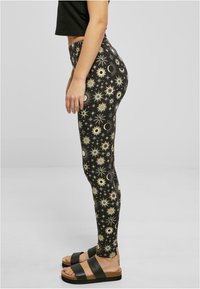 Leggings neri con motivi dorati di sole e luna, con una vita alta e una vestibilità aderente, abbinati a sandali neri a scivolo.
