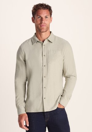 Light green button-up shirt with a textured fabric, a single chest pocket, and a classic collar, worn with dark blue jeans.
