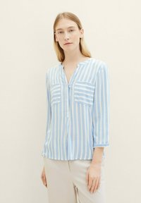 Blusa a rayas azul y blanca con escote en V, mangas largas con puños enrollados, que cuenta con dos bolsillos en el pecho y un corte relajado.