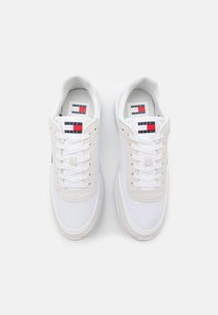 Vita snörkängor i vitt med en strukturerad mocka- och canvasöverdel, med en logotypetikett i rött, vitt och blått på tungan.