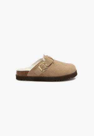 Braune Wildlederclogs mit einer Schnallendetail, weichem Kunstfellfutter, strukturiertem Fußbett und einer braunen Gummisohle mit gerippter Musterung.