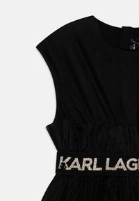 Black dress featuring a structured, cap sleeve design with a textured upper and ruffled waist, accented by a glittery branded waistband.