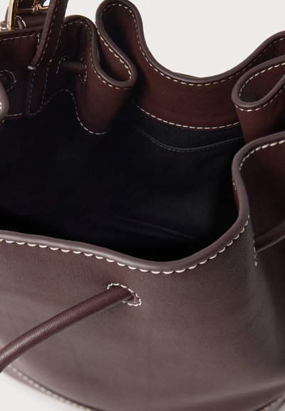 Hnedá kožená kabelka v tvare vedra s textúrovaným povrchom, vybavená mäkkým vnútrom a kontrastným bielym šitím pozdĺž okraja. Otvorený vrchný dizajn.