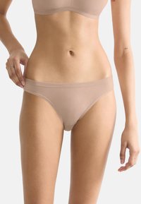 Beige hipsterondergoed gemaakt van gladde stof, met een brede tailleband en minimale bedekking, die een strakke uitstraling benadrukt.