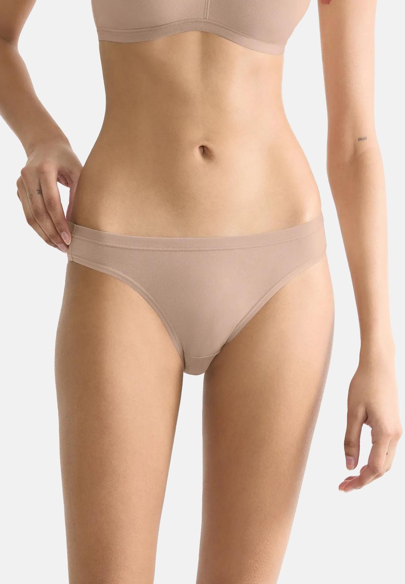 Beige hipsterondergoed gemaakt van gladde stof, met een brede tailleband en minimale bedekking, die een strakke uitstraling benadrukt.