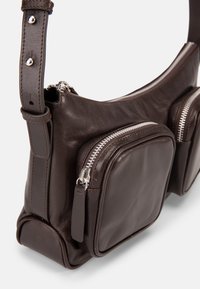Tmavě hnědá kožená kabelka přes rameno se dvěma předními kapsami na zip a nastavitelným popruhem se stříbrnými kovovými doplňky.