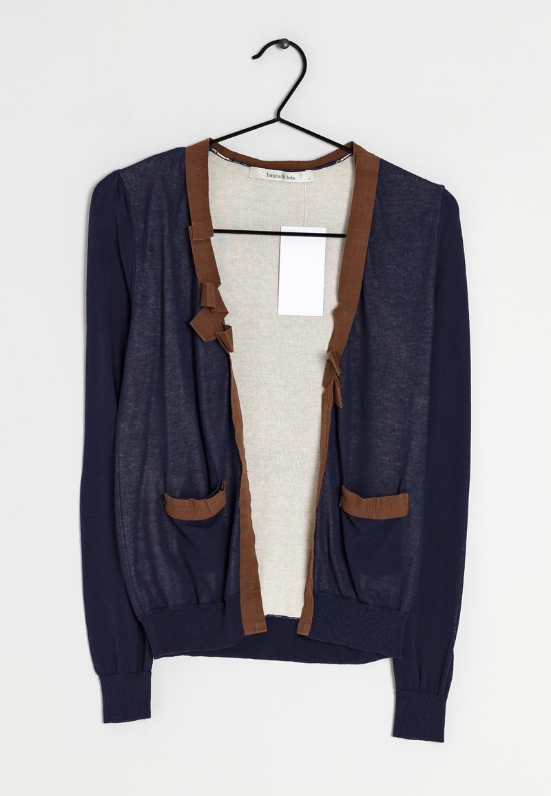 Laivastonsininen neuletakki, jossa ruskea reunus, kaksi etutaskua, kevyt kangas, pitkät hihat ja hillitty tekstuuri. Ripustettuna mustaan koukkuun.