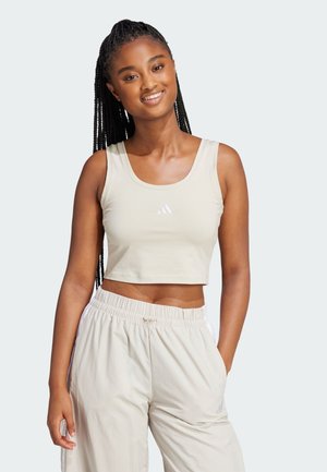 Top corto beige con spalline larghe e scollatura rotonda, caratterizzato da un piccolo logo Adidas bianco sulla parte anteriore. Tessuto dalla texture liscia.