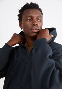 Sudadera con cremallera de color azul marino oscuro, con cuello alto, puños acanalados y un bolsillo frontal. La tela parece suave y ligeramente texturizada.