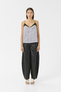 Camisola in satin nero e grigio con spalline sottili, abbinata a pantaloni in pelle nera larghi e scarpe aperte di colore chiaro.