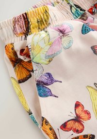 Pantalon enfant à taille élastique avec des imprimés papillons colorés sur tissu rose clair, montrant des coutures détaillées et la texture.