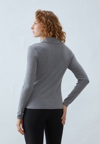 Grijze geribde coltrui met lange mouwen, aansluitend ontwerp en subtiele textuur. Gecombineerd met zwarte legging, getoond vanuit de achterkant.